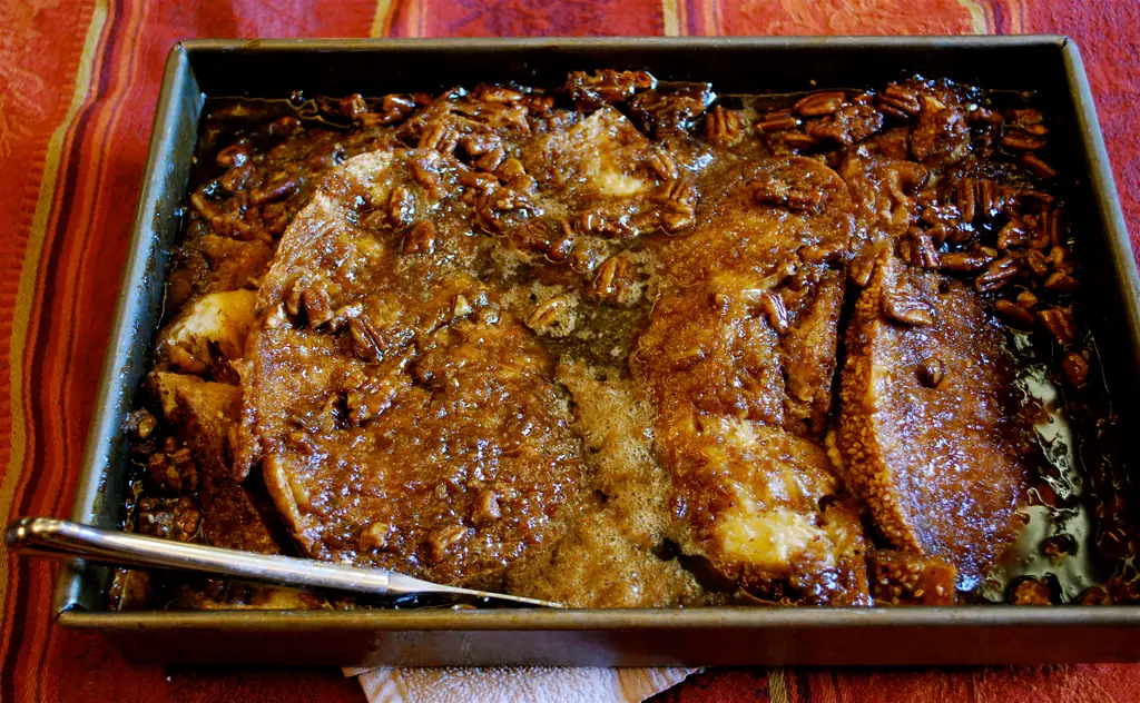 A rectangular tin of browned thick bread slices with a glossy pecan topping and a serving spoon.