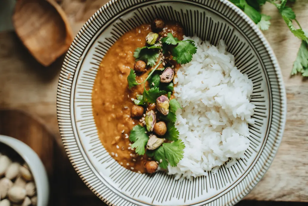 White rice beside orange lentil curry, topped with chickpeas, green pistachios, sesame seeds and coriander leaves.