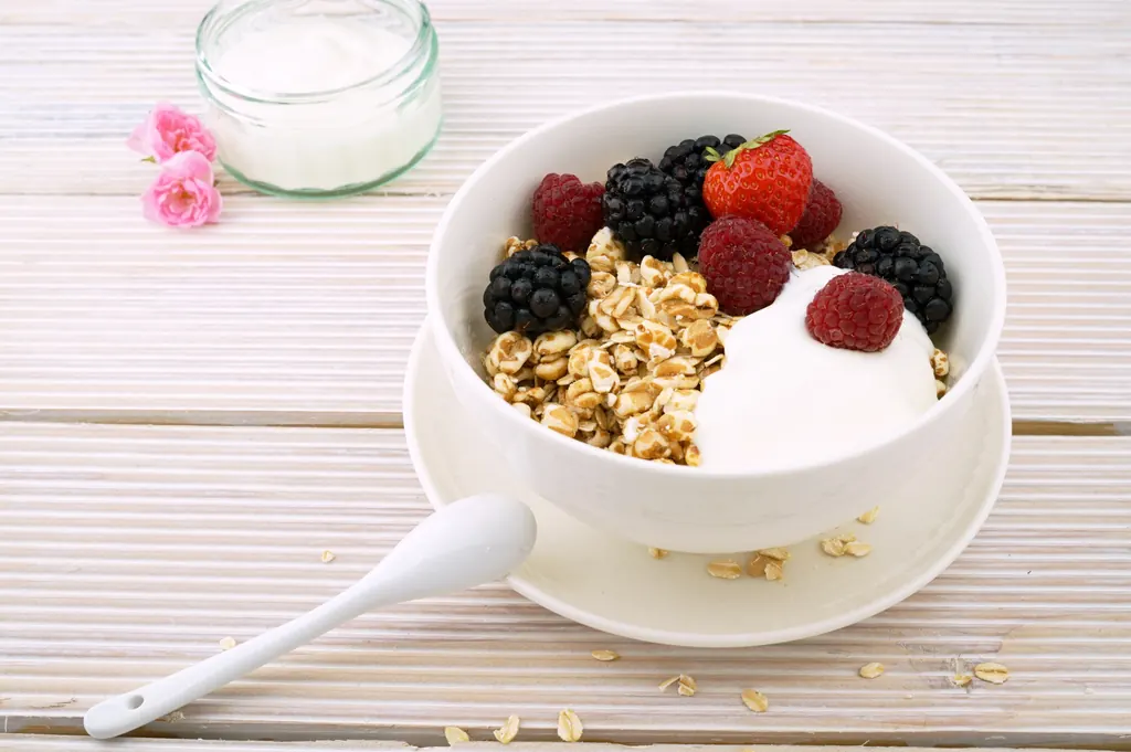 A bowl of yoghurt and muesli topped with strawberries, raspberries and blackberries.