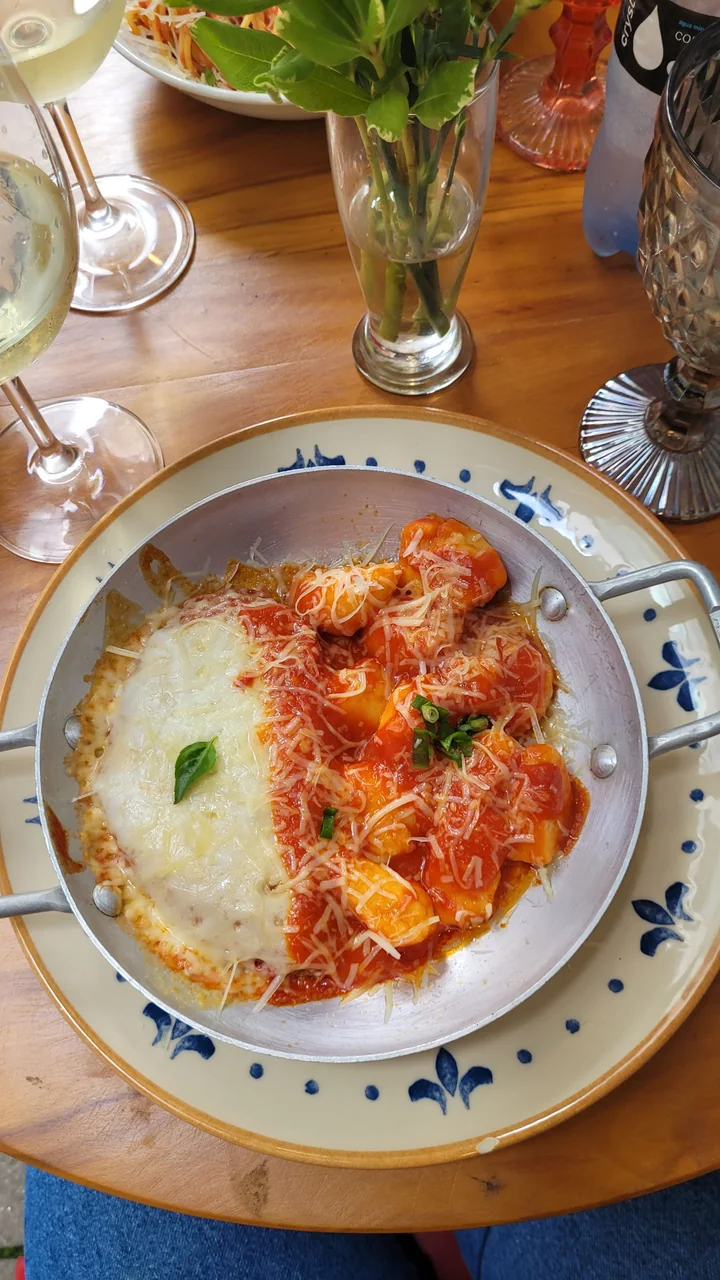 Gnocchi in red tomato sauce in a round pan, topped with melted and grated pale cheese and basil, on a dining table.
